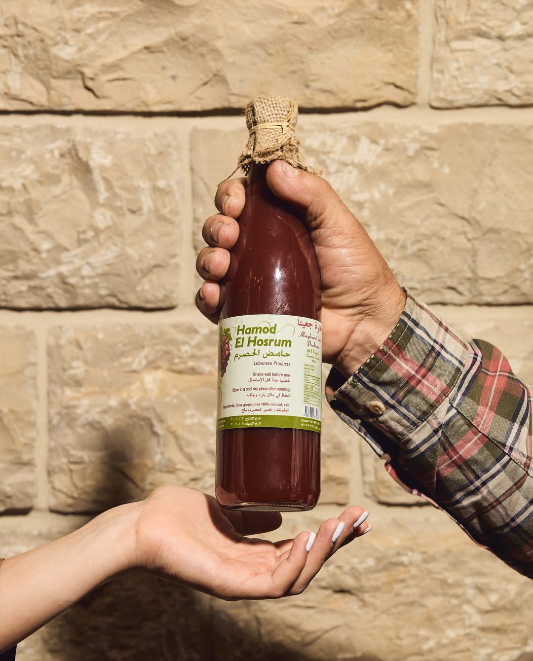 Father handing Hamod El Hosrum bottle to daughter against stone wall